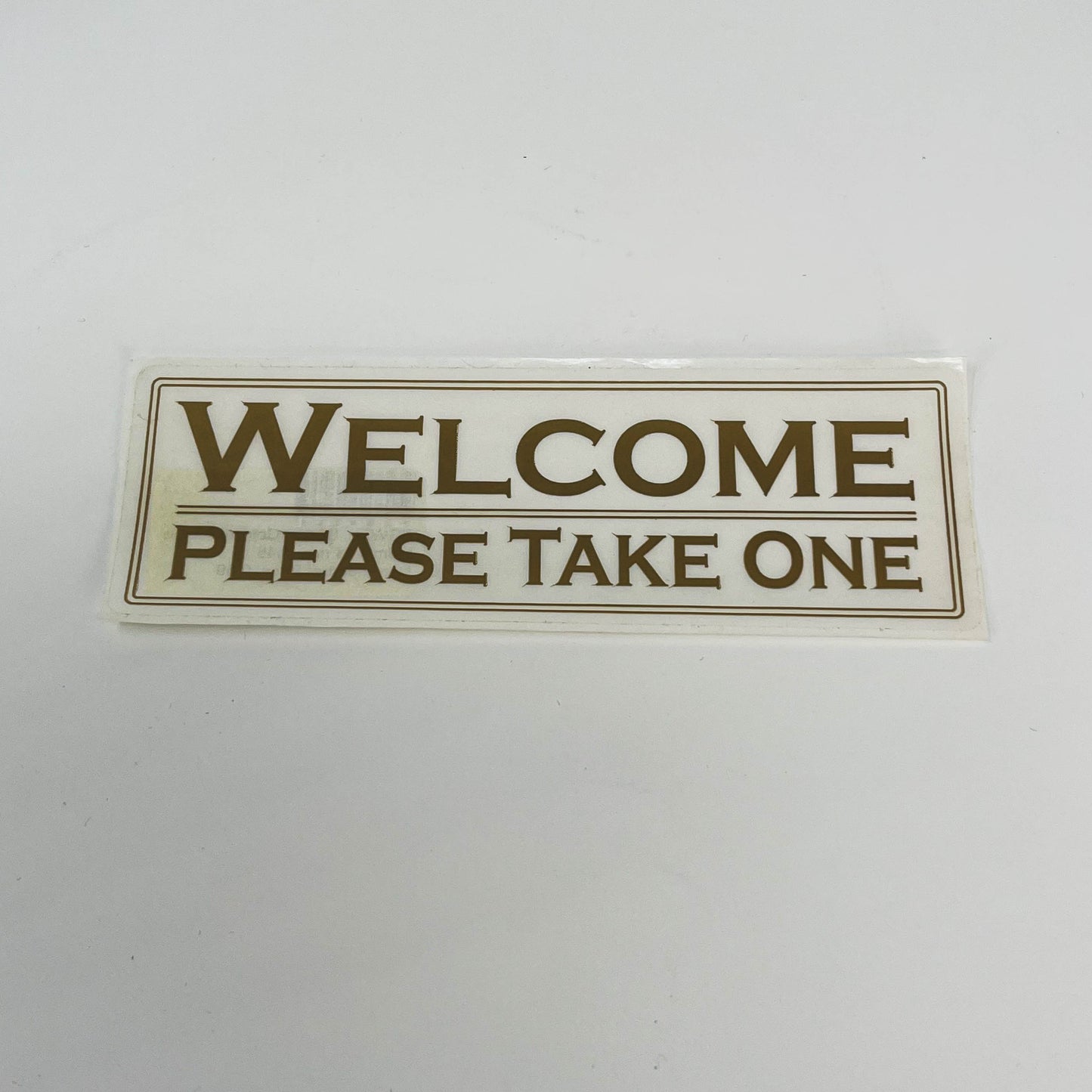 Sticker Welcome Please Take One white with gold letters 2"x 6" (SGWEL)